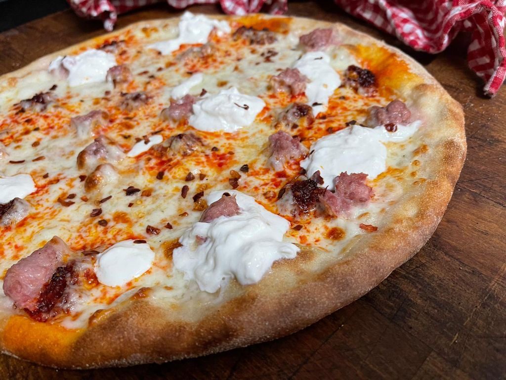 Pizza con salsiccia e stracciatella appena uscita dal forno, su un tagliere di legno